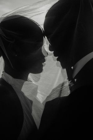 Black and white silhouette of a bride and groom facing each other under a wedding veil.