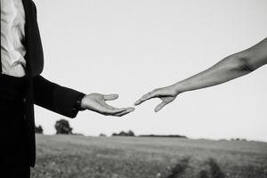 Black and white photo of two hands nearly touching in a field, evoking romance and connection.