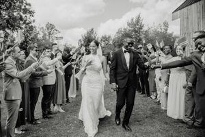 Black and white photo of a bride and groom walking through a celebratory send-off line of cheering wedding guests outdoors.