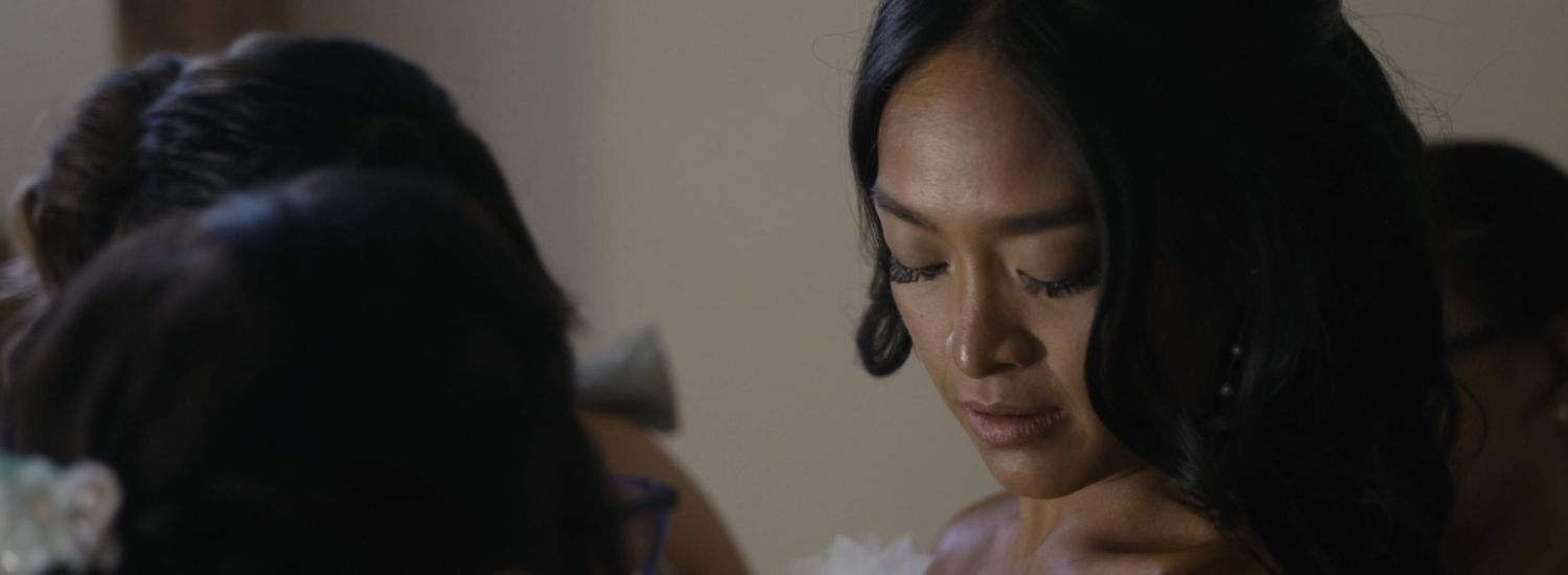 A young Asian woman in elegant attire gazes downward thoughtfully at a formal event.