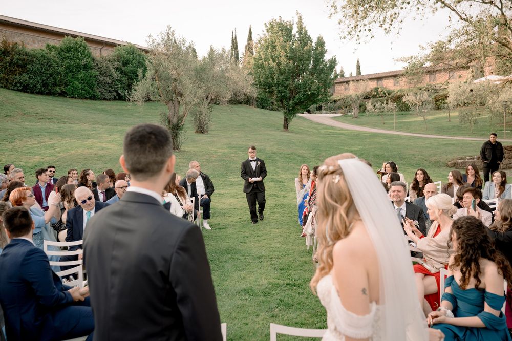 Outdoor wedding ceremony on lush green lawn with bride and groom at altar, guests seated in white chairs, Tuscany villa backdrop.