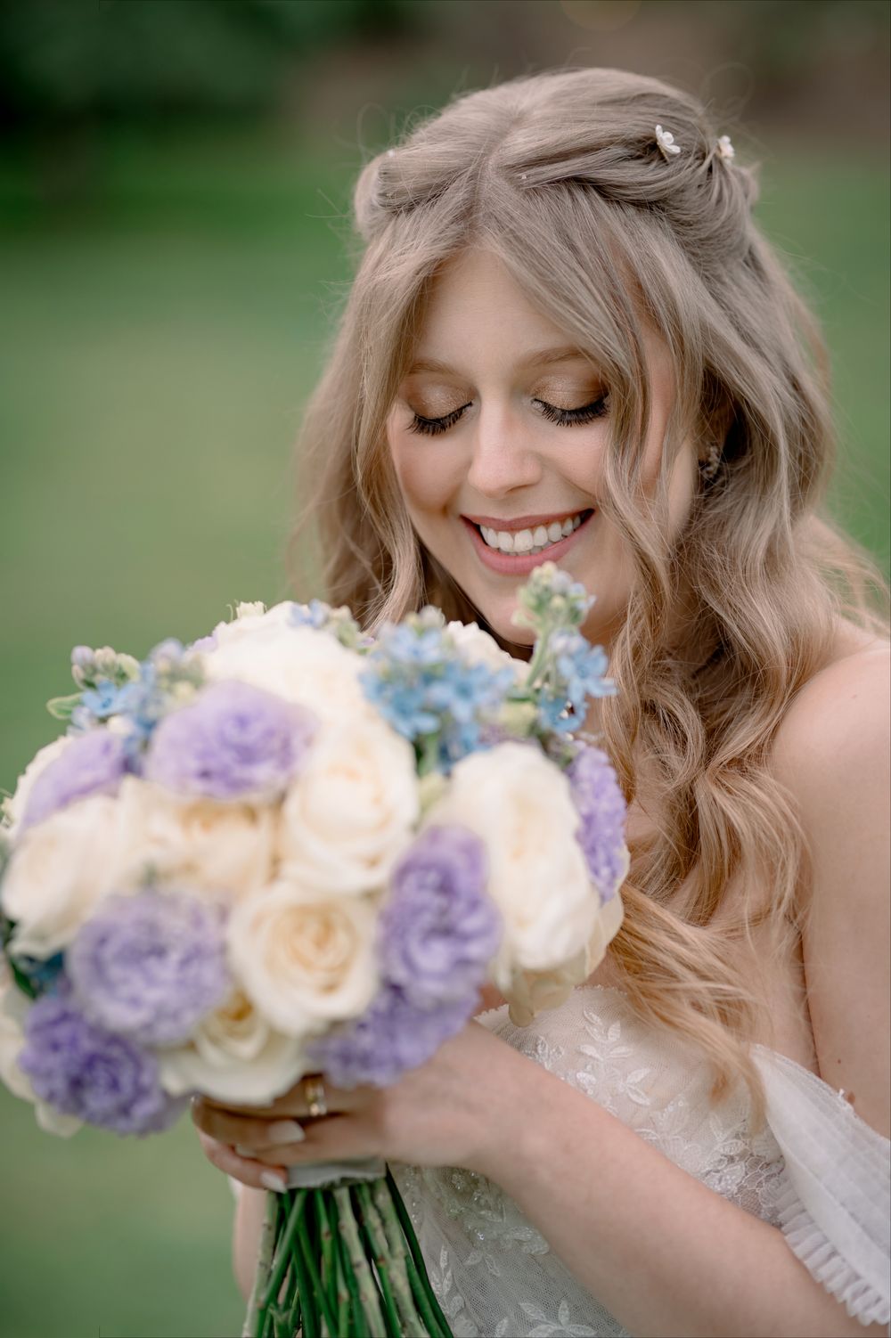 Smiling bride holding a bouquet of purple and white roses with blue flowers on her wedding day.