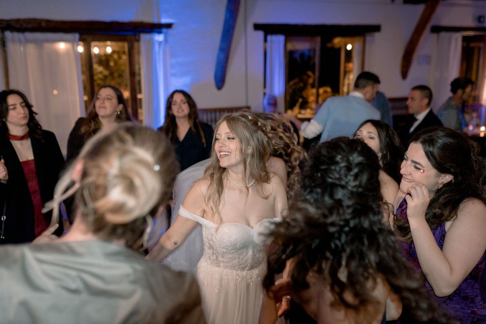 Bride in white gown dancing joyfully with guests at a lively wedding reception party.
