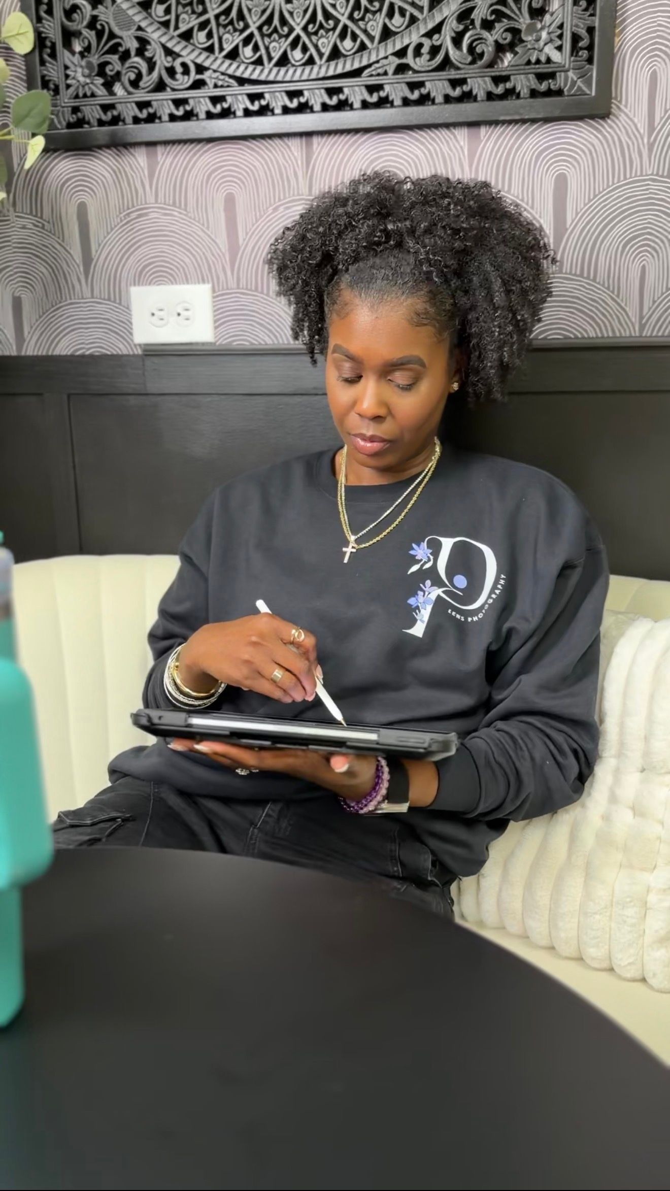 Woman in black sweatshirt writing on tablet with stylus while seated on couch in modern interior.