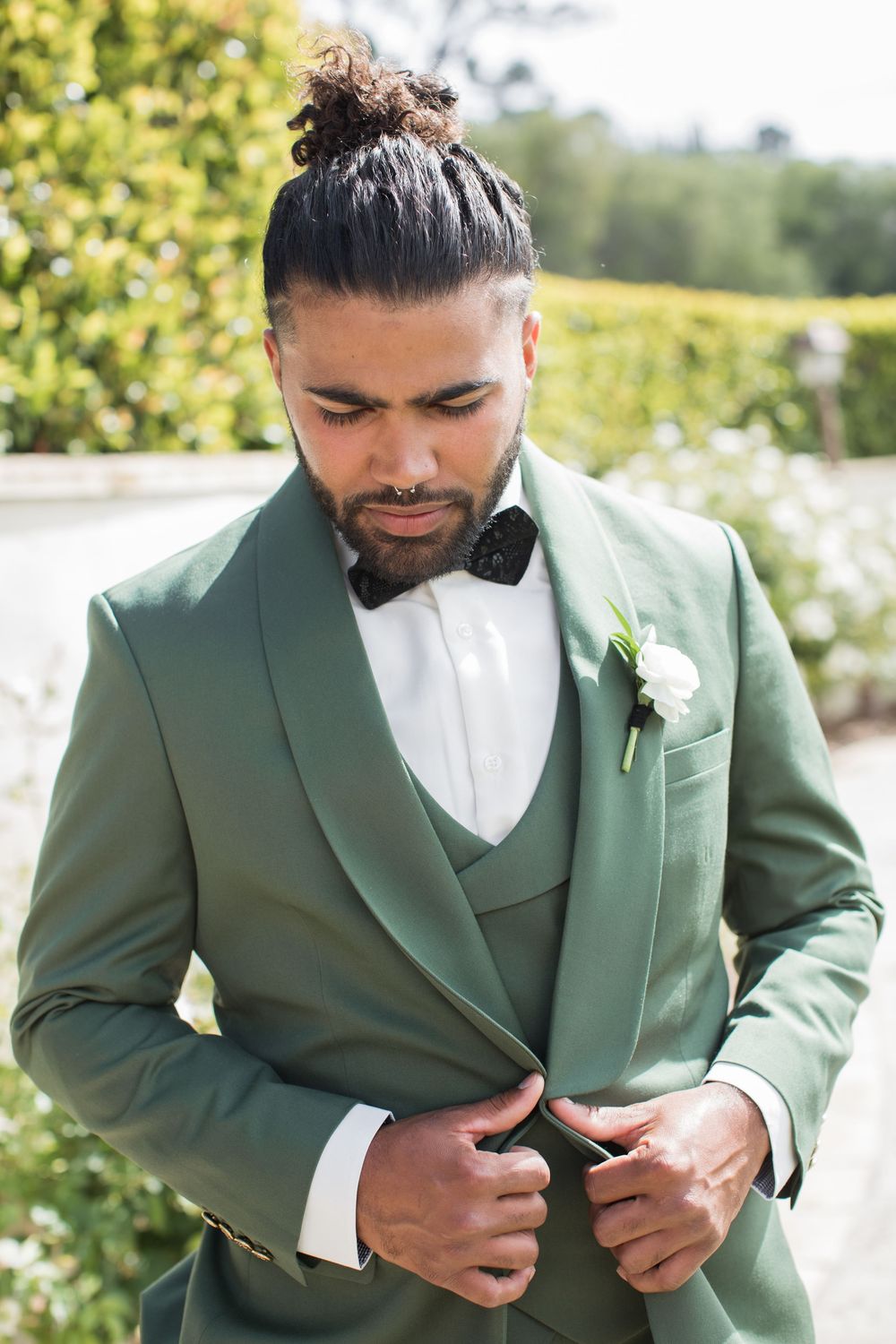 Groom in sage green tuxedo with bow tie and white boutonniere outdoors.
