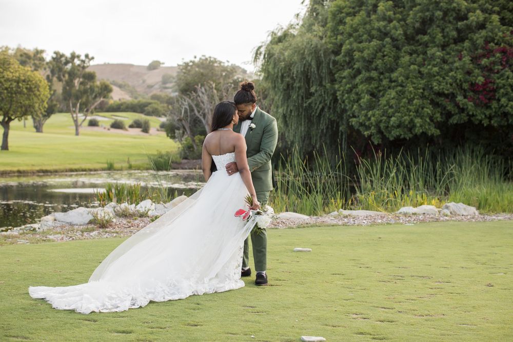 Bride and groom share a romantic moment on a lush green golf course with a scenic pond backdrop.