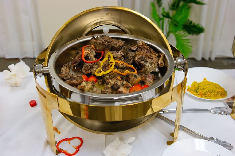 Gold chafing dish filled with braised meat, bell peppers, and garnishes at a buffet catering event.