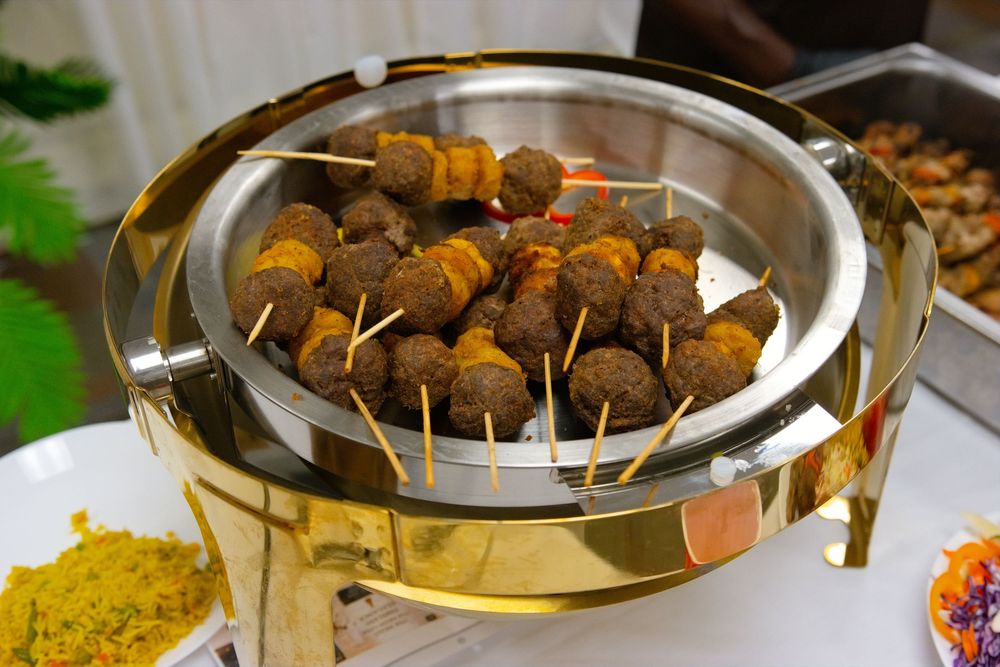 Golden chafing dish filled with skewered meatballs and kebabs at a buffet catering event.