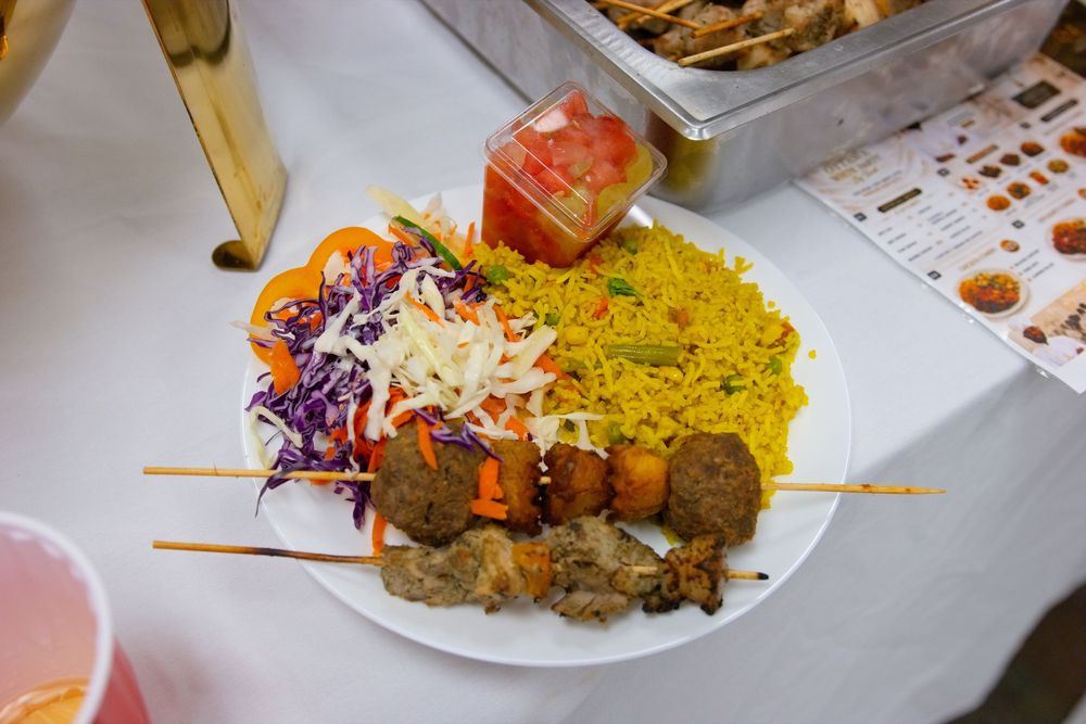 Middle Eastern plate with kebab skewers, falafel, yellow rice, coleslaw, and a cup of fresh salsa.