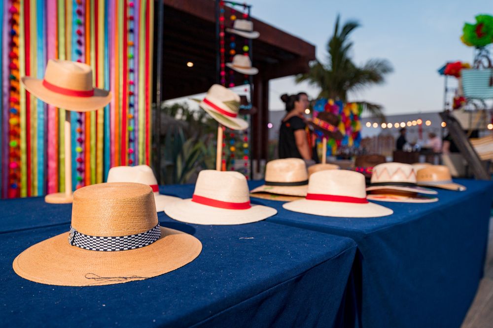 Colorful straw hats displayed on a blue table at a vibrant outdoor Mexican market with festive decorations.
