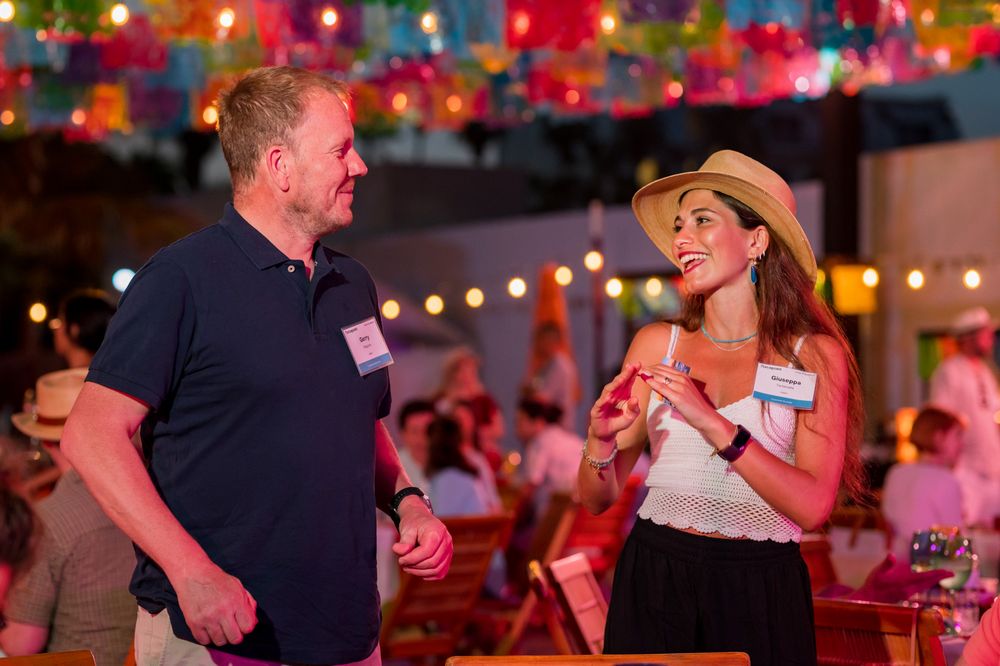 Two people networking at a festive outdoor party with colorful paper decorations and string lights overhead.