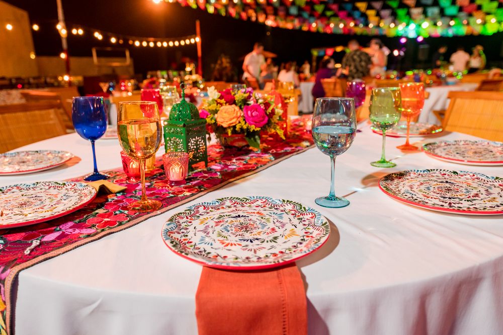 Colorful fiesta table setting with decorative plates, vibrant glassware, and floral centerpieces on a white tablecloth.