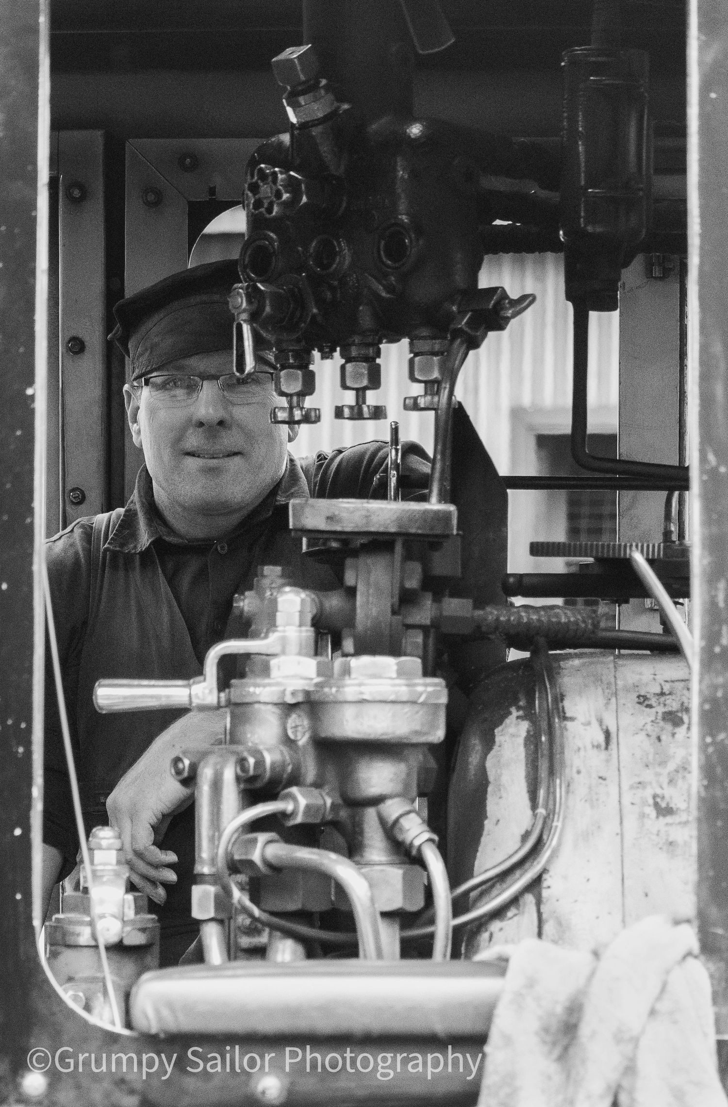 Black and white photo of a smiling engineer operating machinery in a locomotive cab.