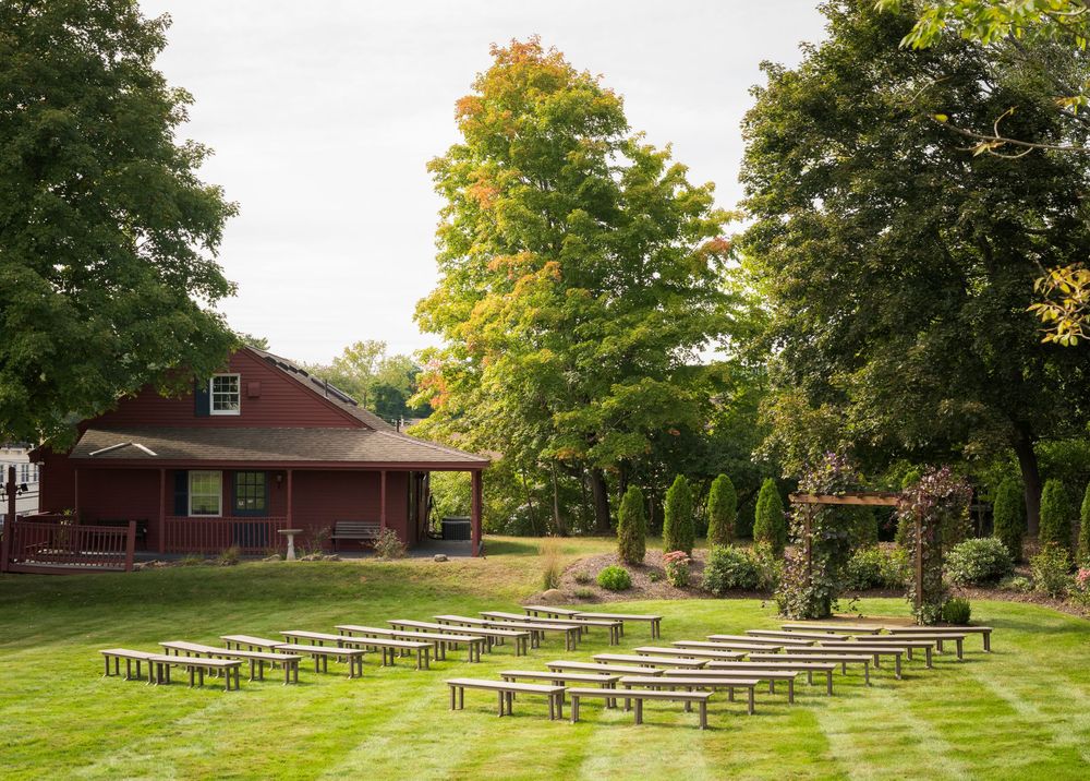 Rows of wooden benches arranged on a green lawn for an outdoor wedding ceremony near a red barn.