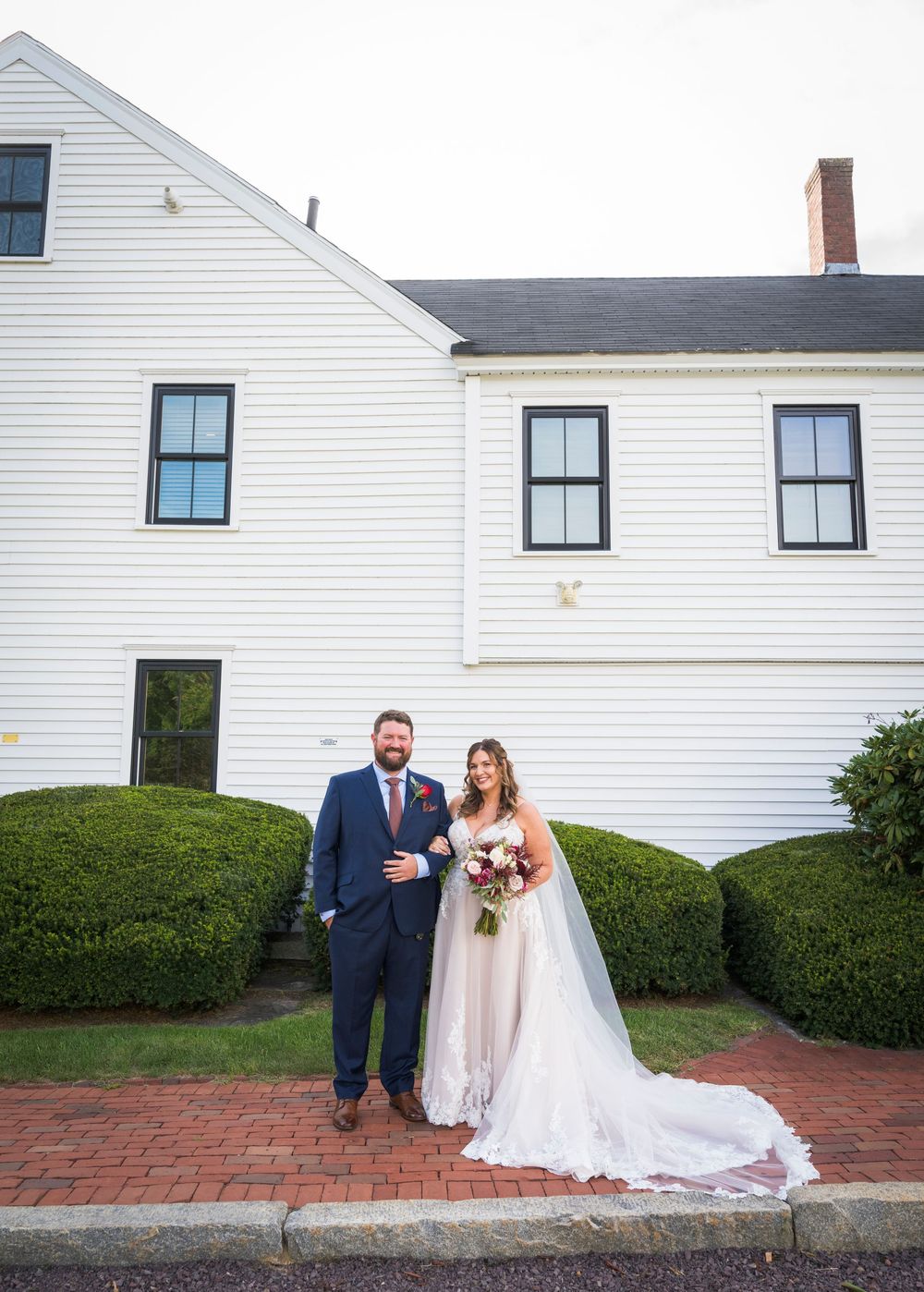 Bride and groom posing together in front of a white colonial building on their wedding day.