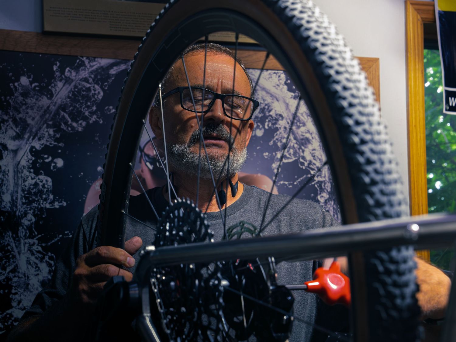 The owner of Velocity Multi Sport & Cycling focused on a mountain bike wheel, framed through the spokes in his Janesville shop.