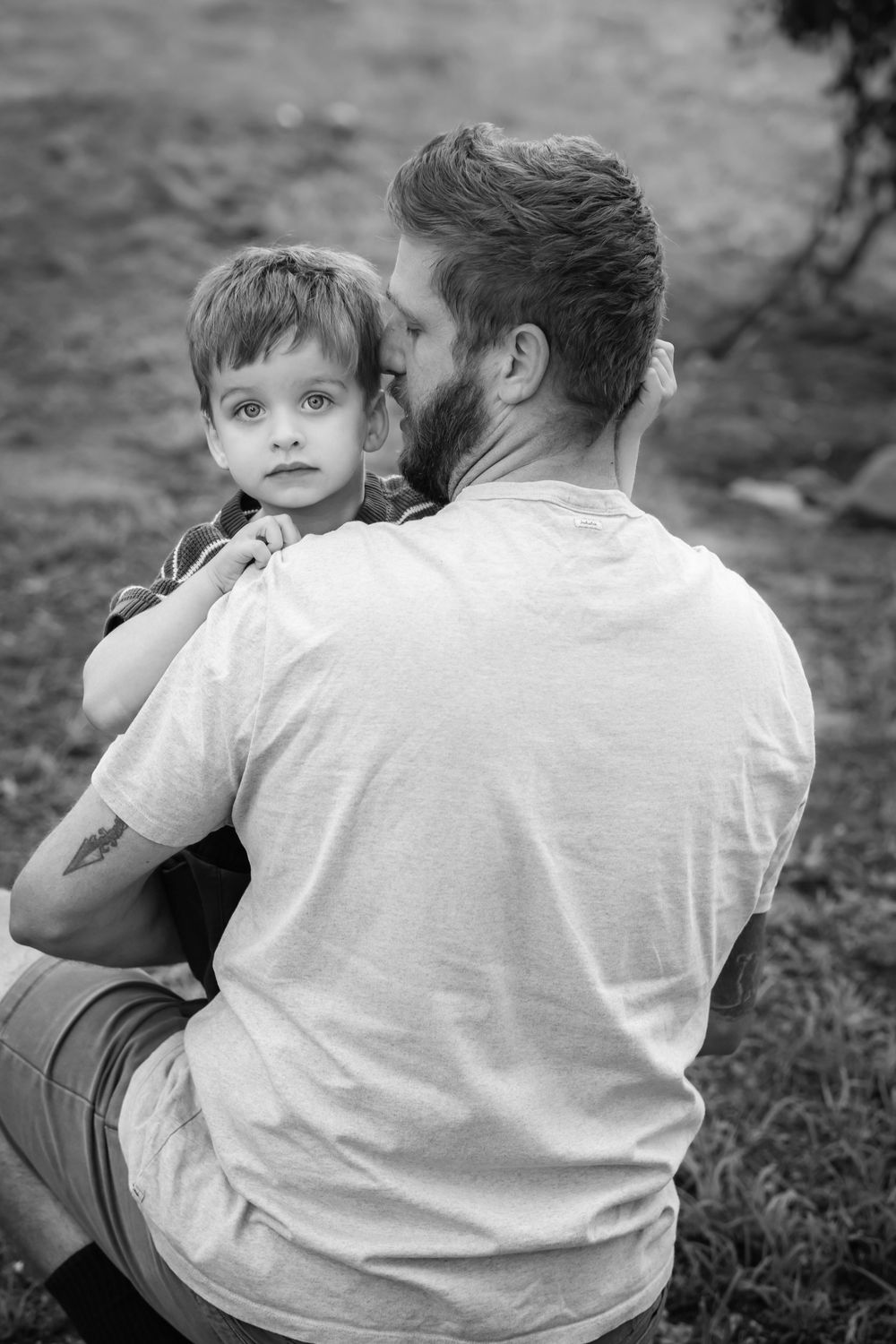 Black and white photo of a bearded father kissing his young son on the cheek outdoors.