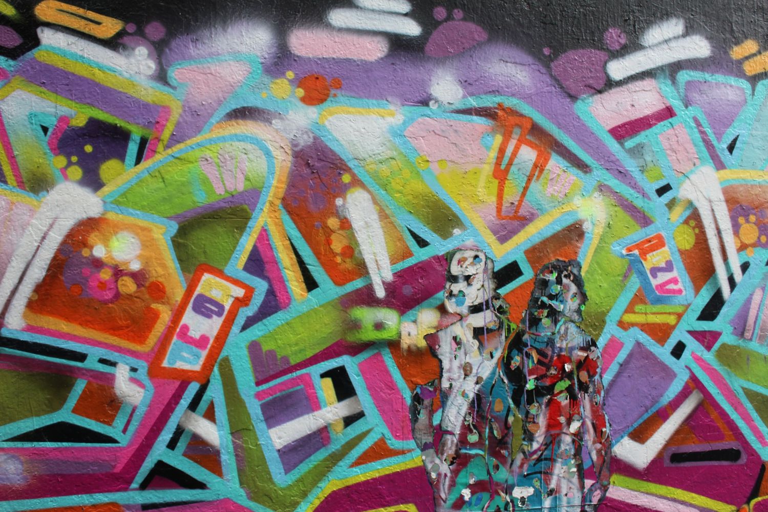Colorful graffiti mural featuring geometric shapes with two robot figurines in front.