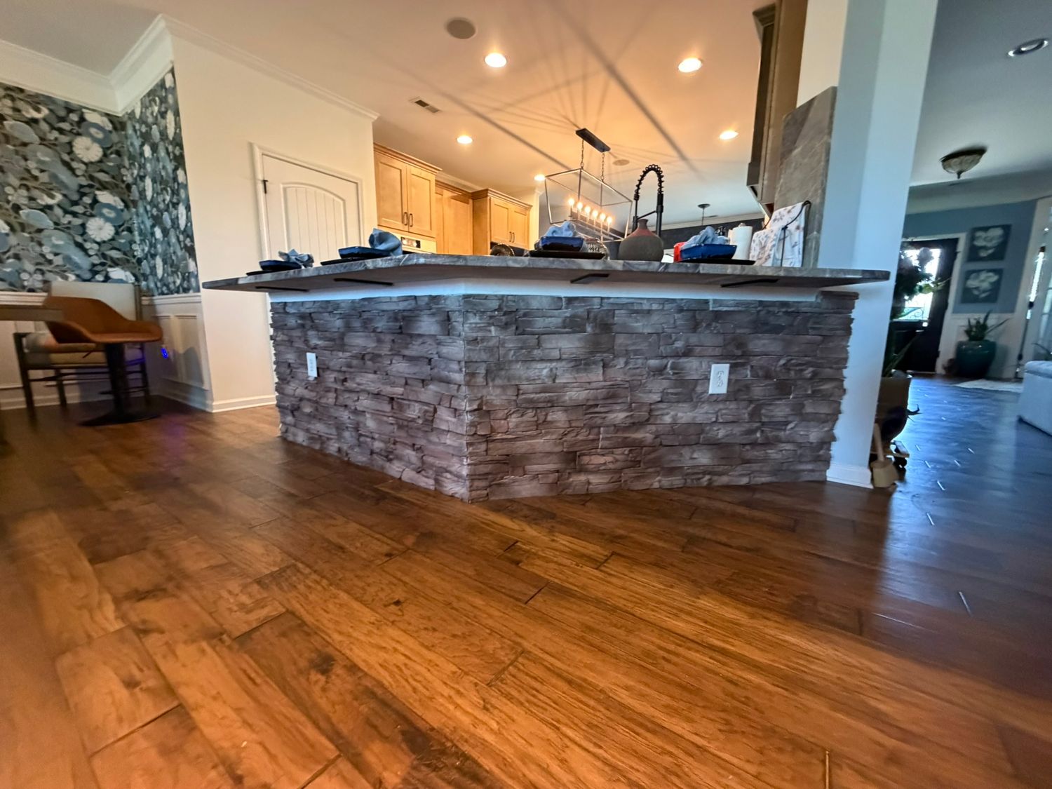 Stone-clad kitchen island with dark granite countertop and rich hardwood flooring.