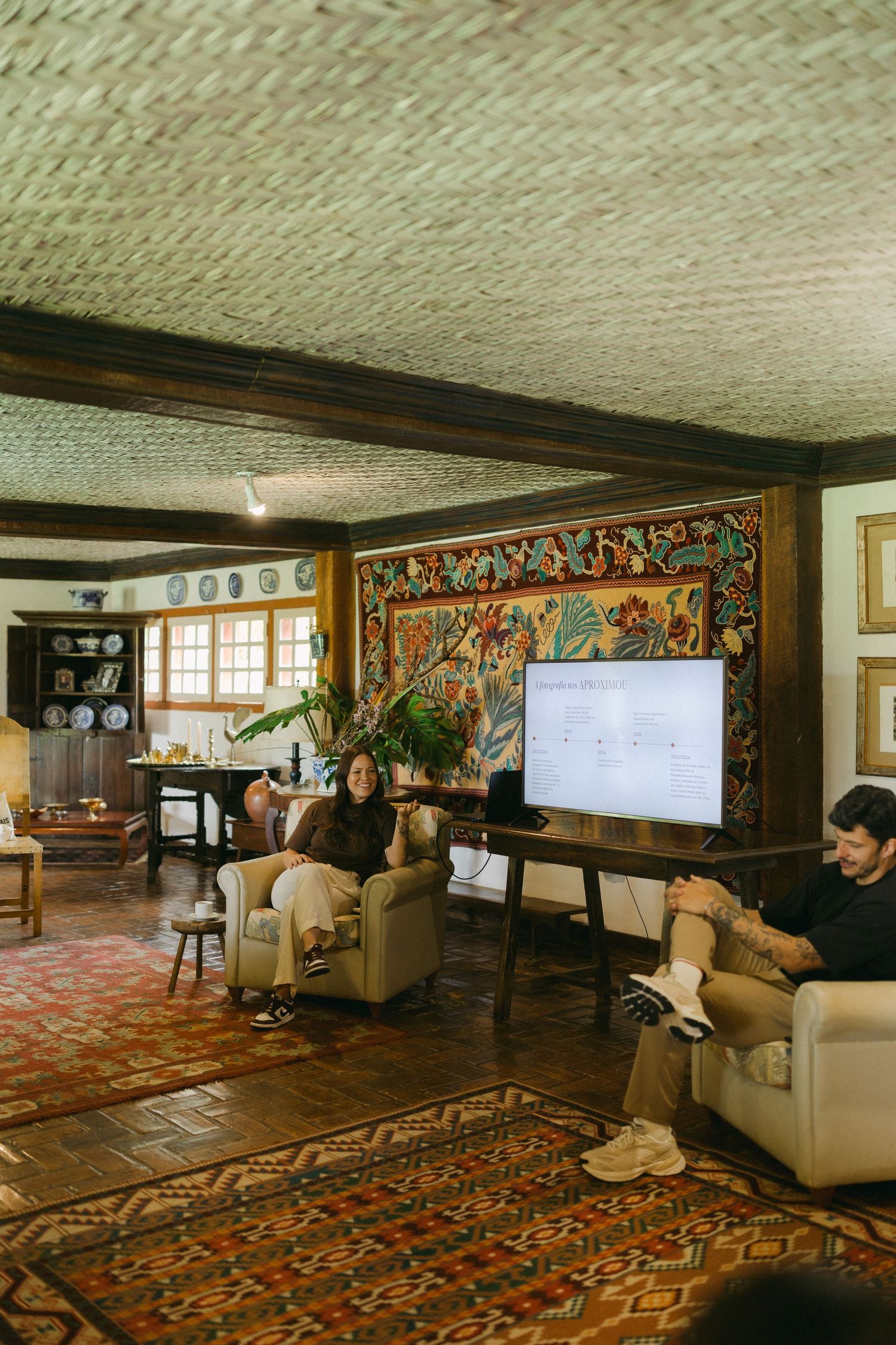 People gathered in a rustic room with colorful tapestry, patterned rugs, and a presentation screen during a meeting.