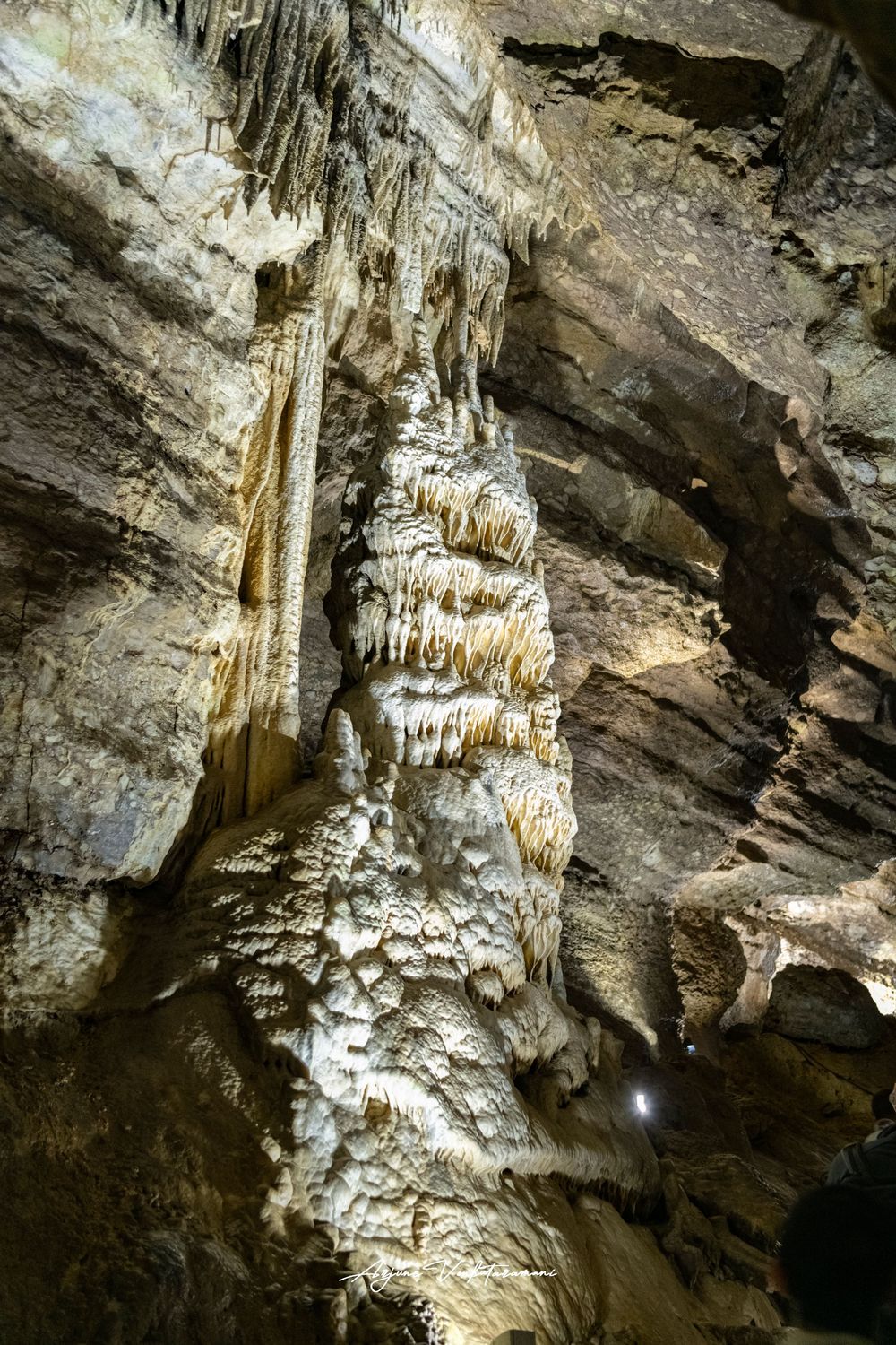 Massive stalactite formation inside a limestone cave with dramatic rock textures and artificial lighting below.