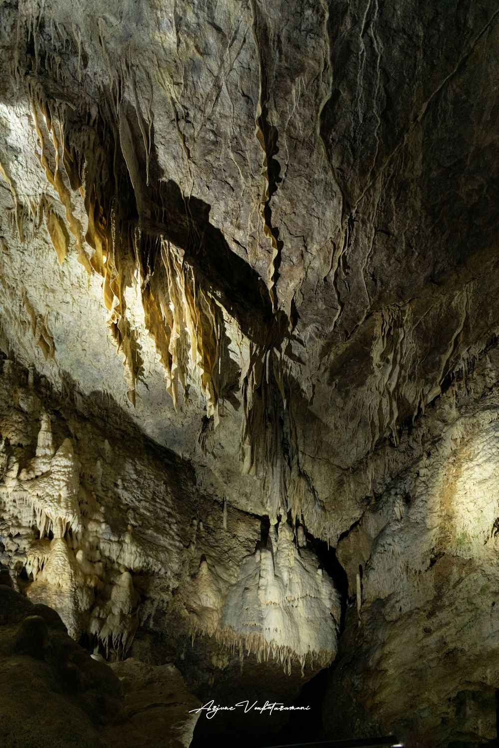 Stunning cave interior with golden stalactites hanging from rocky ceiling, illuminated by dramatic natural lighting.