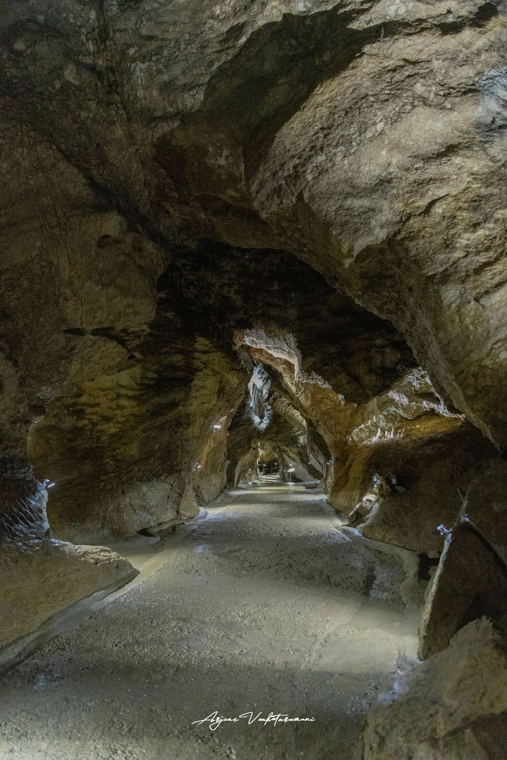 Illuminated cave tunnel with rocky walls and pathway leading deep into a natural limestone cavern.