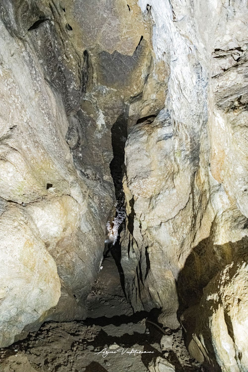 Narrow rocky cave passage with dramatic stone walls and stalactites in a natural limestone cavern.