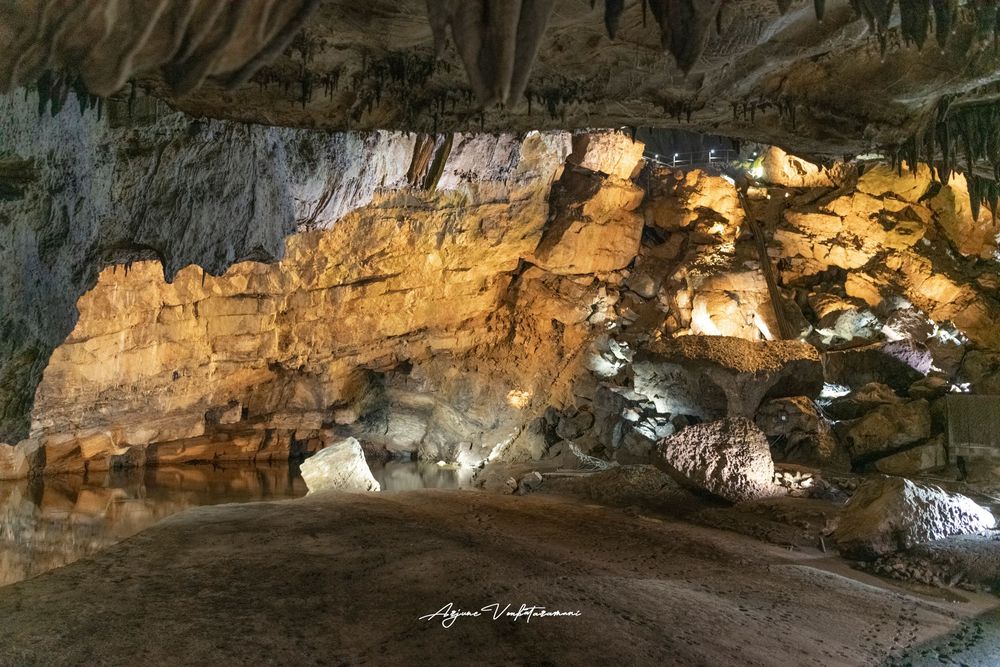 Illuminated cave interior showcasing layered golden rock formations and stalactites with dramatic lighting.