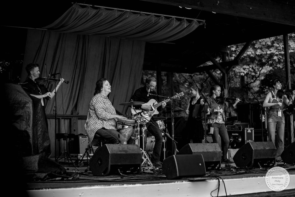 Black and white photo of a live band performing on an outdoor stage with multiple musicians playing instruments.