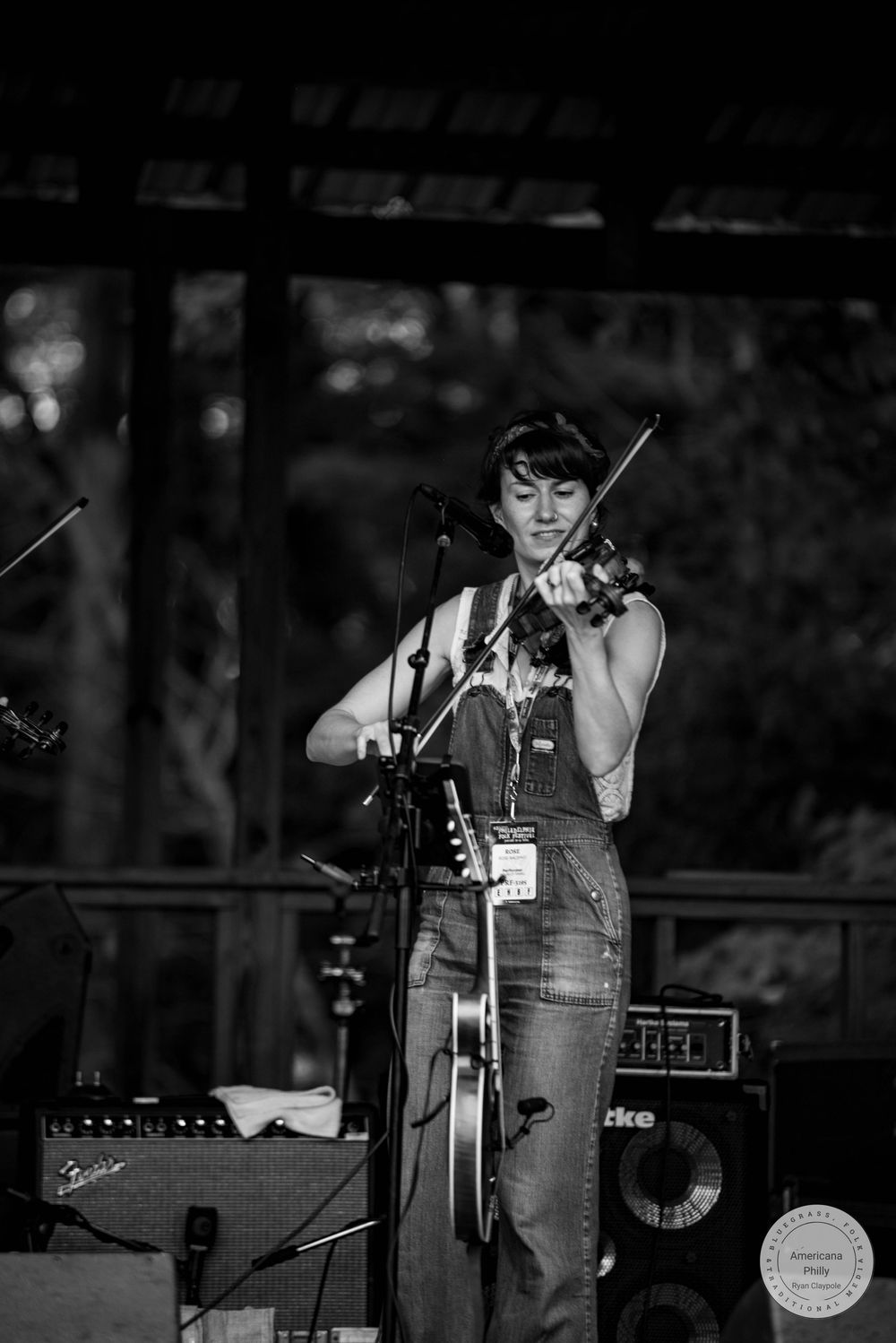 Woman in overalls playing violin on stage in black and white concert photography.