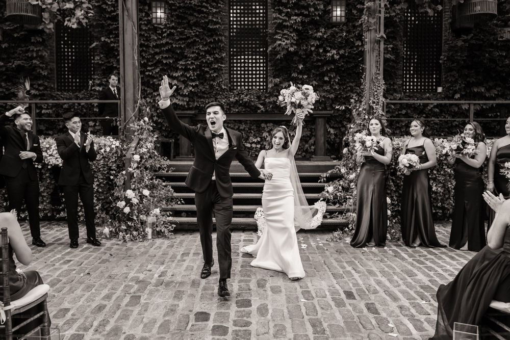 Black and white photo of newlyweds cheering as they walk past their wedding party at The Foundry, Long Island City, NY
