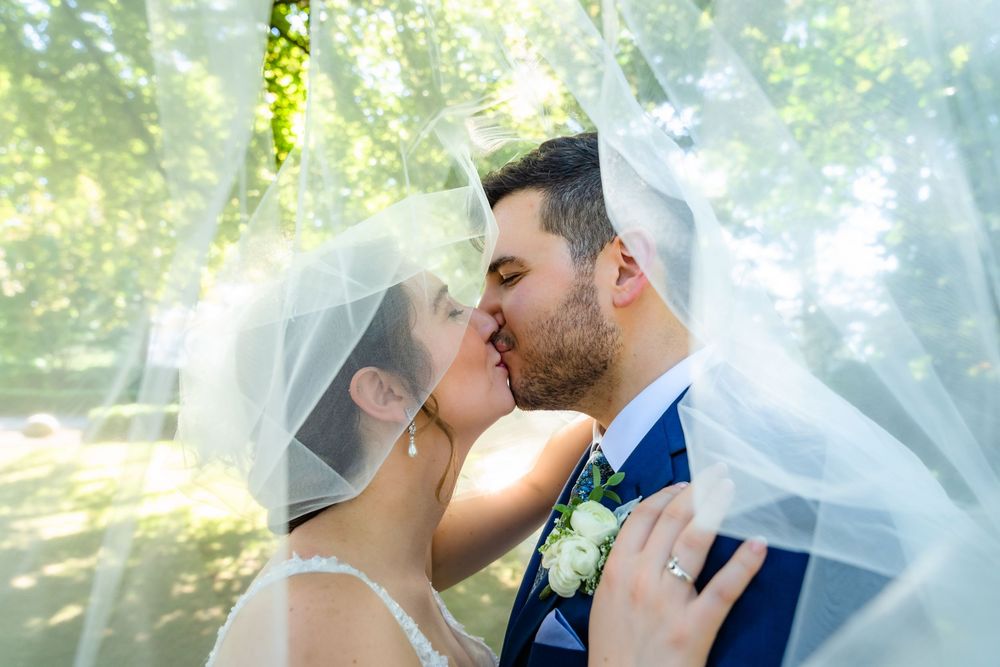 Bride and groom kiss under her veil among sunlit trees at Burr Homestead, Fairfield, CT