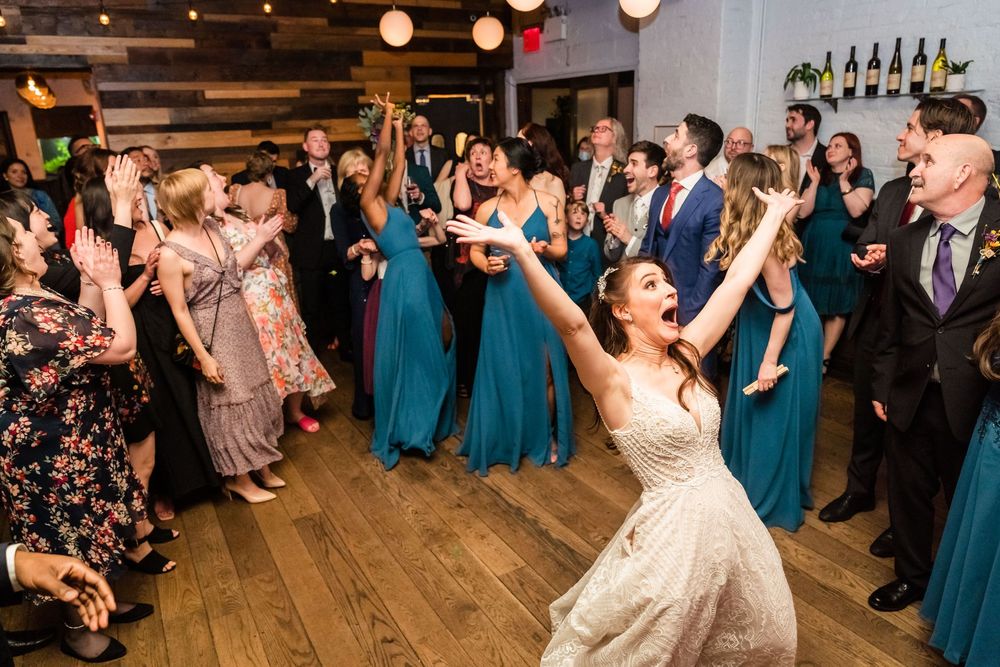 Bride throws her arms up on the dance floor among bridesmaids in teal at Brooklyn Winery, Brooklyn, NY