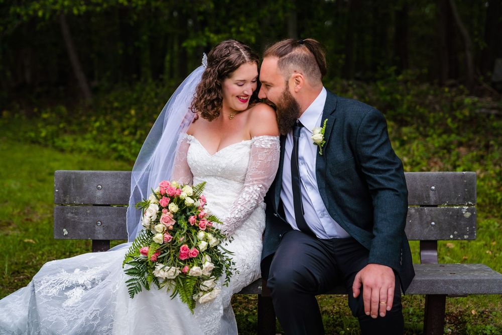 Groom kisses the bride's shoulder as she laughs on a bench at Earthplace, Westport, CT