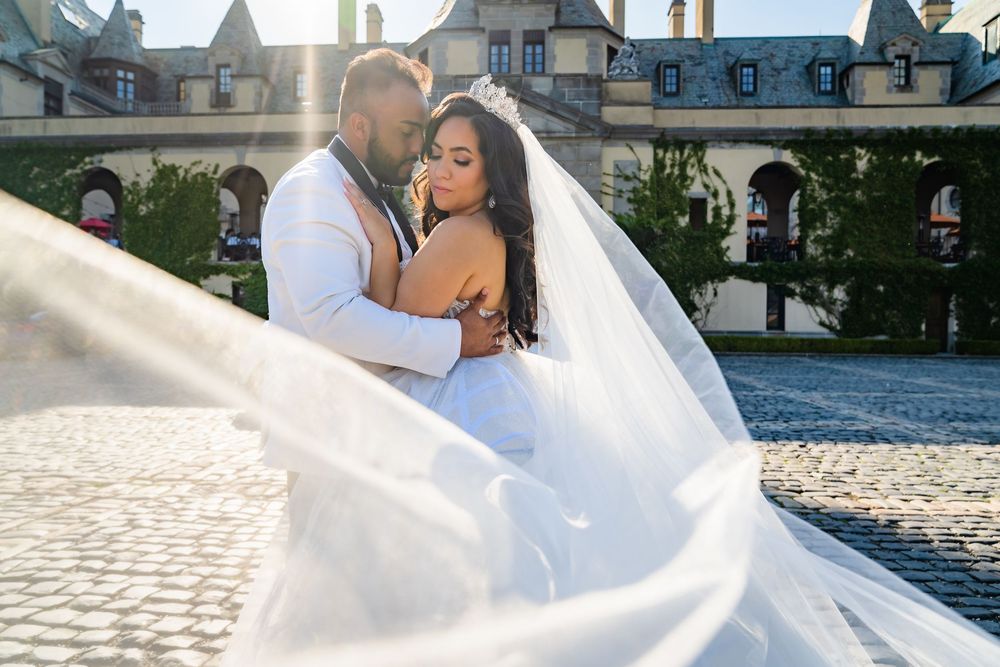 Bride's veil sweeps across the frame as the couple embrace in the cobblestone courtyard of Oheka Castle, Huntington, NY