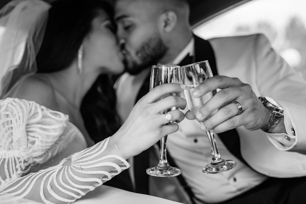 Black and white close up of a couple kissing as they touch champagne glasses, Oyster Bay, NY wedding