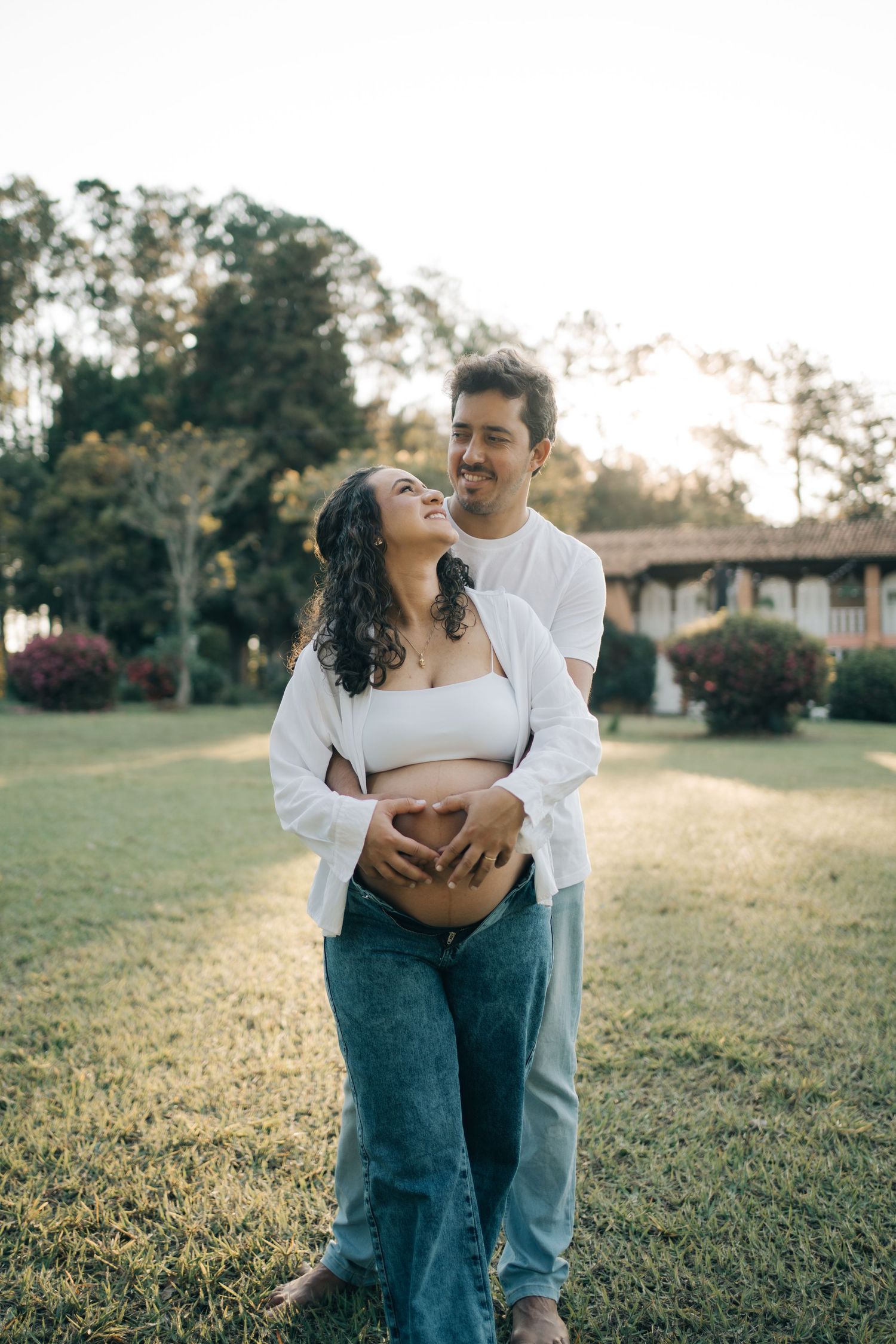 Bruno abraça Liliana por trás enquanto os dois sorriem e seguram a barriga na Fazenda Vintém.