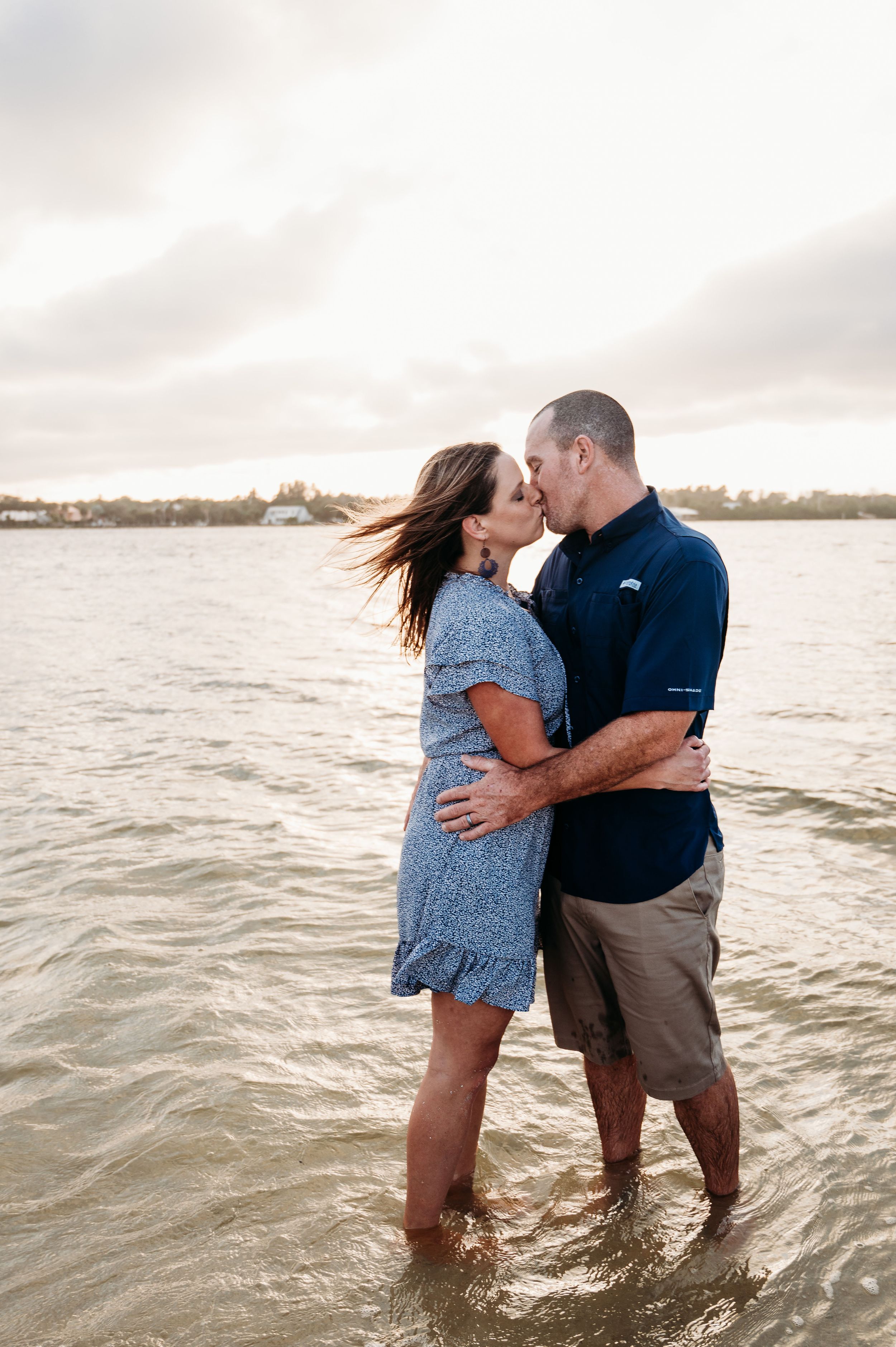 Romantic couple embracing in shallow ocean water at sunset with waves lapping at their feet.