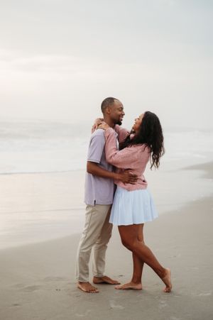 A romantic couple embraces while dancing barefoot on a peaceful beach at sunset.