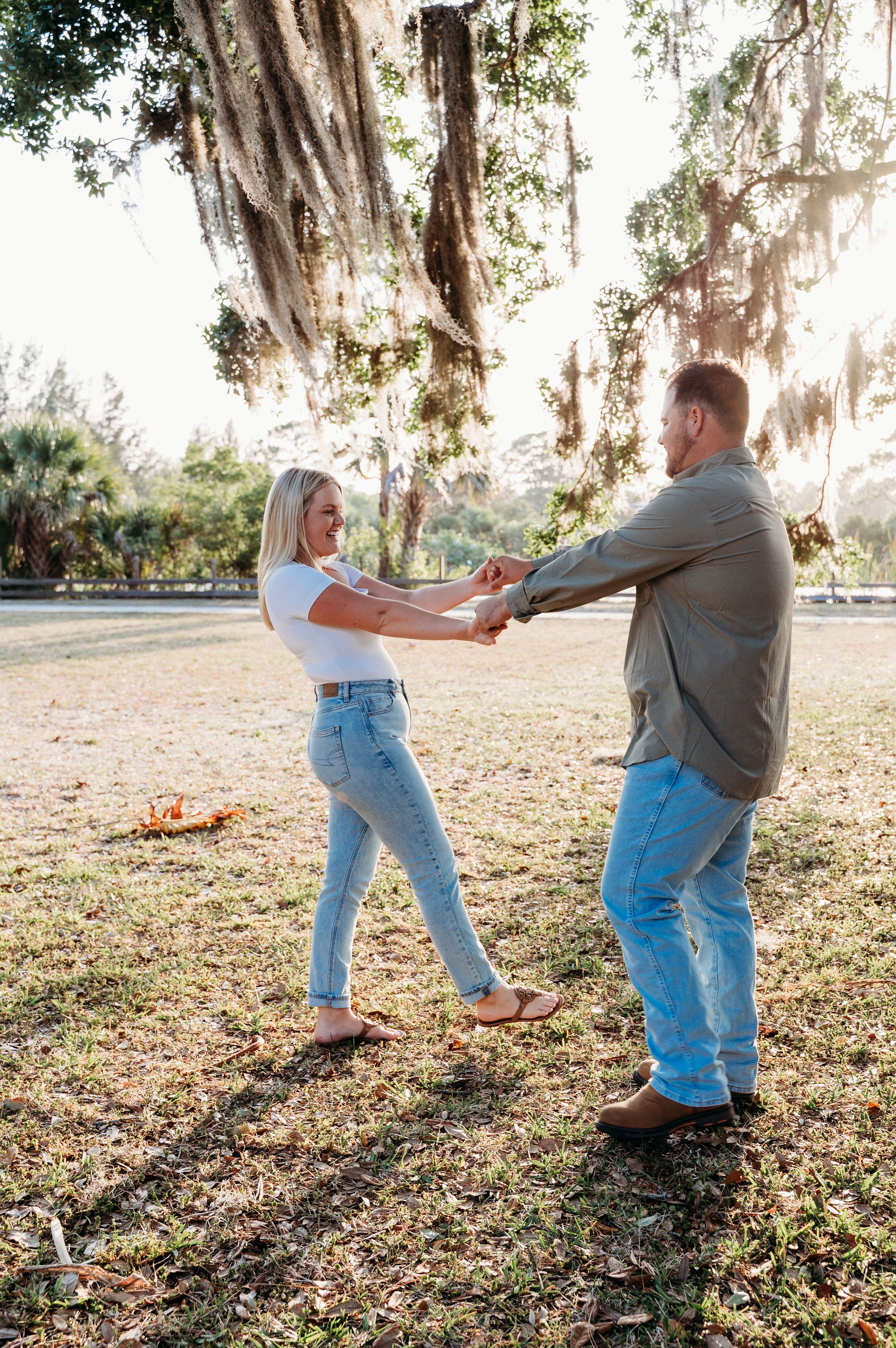 A couple dances together under Spanish moss draped trees at sunset in a romantic outdoor setting.