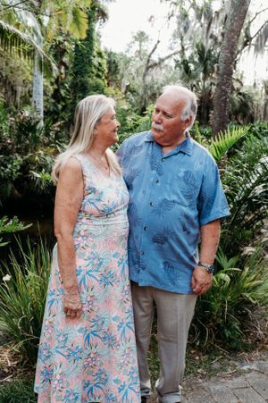 A loving senior couple shares a tender moment together while standing in a lush tropical garden setting.