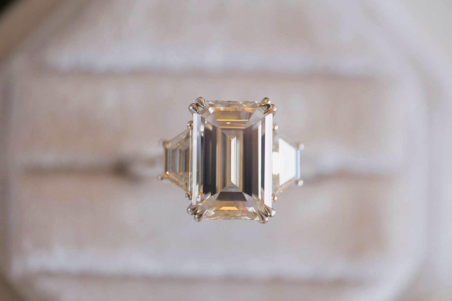 Elegant three-stone engagement ring featuring a large emerald-cut diamond center with trapezoid side stones in a white gold setting.