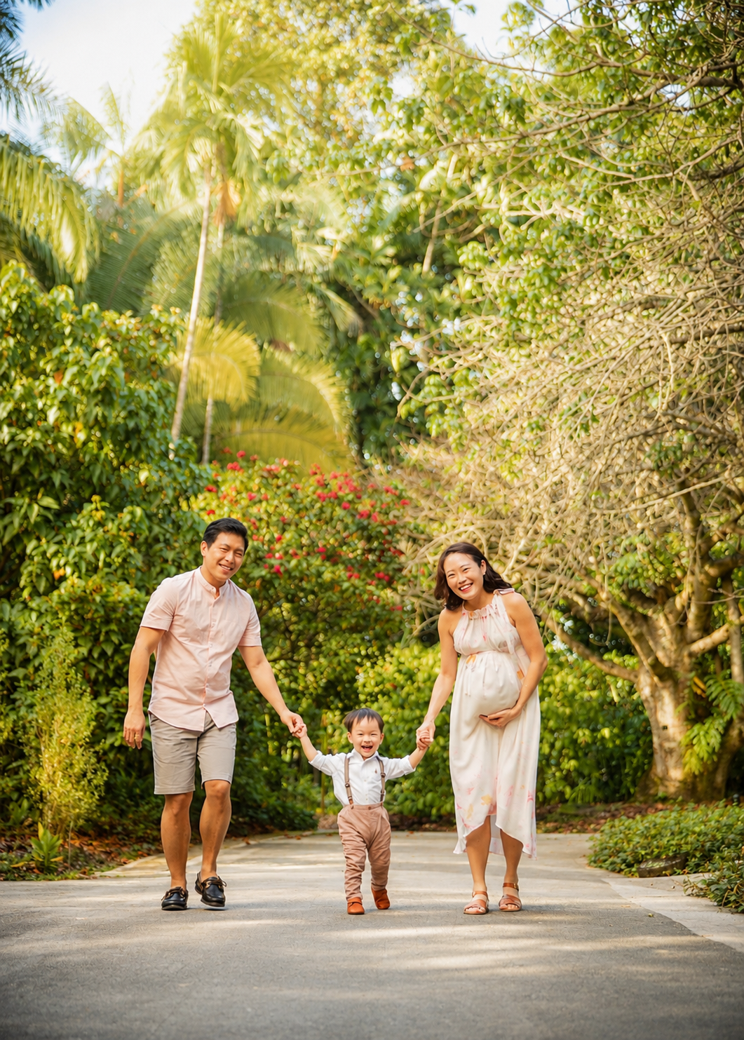 Happy Asian family walking together on a sunny path, father and pregnant mother holding toddler's hands.