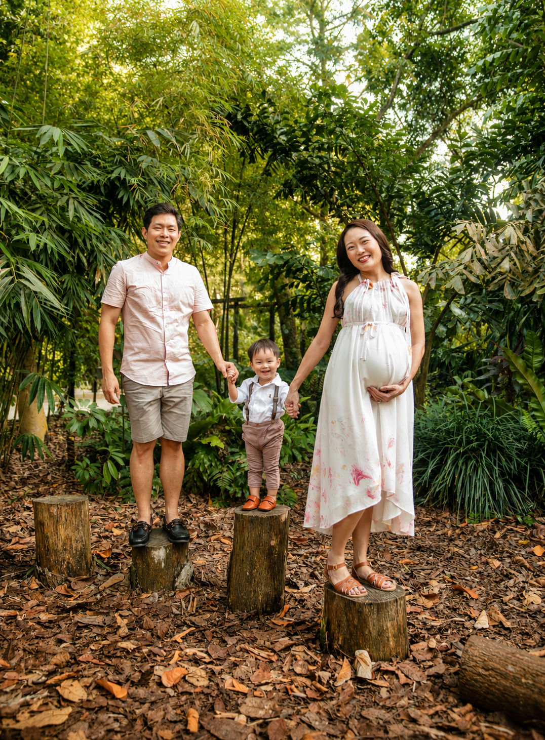 Asian family maternity photo standing on tree stumps in a bamboo forest setting.