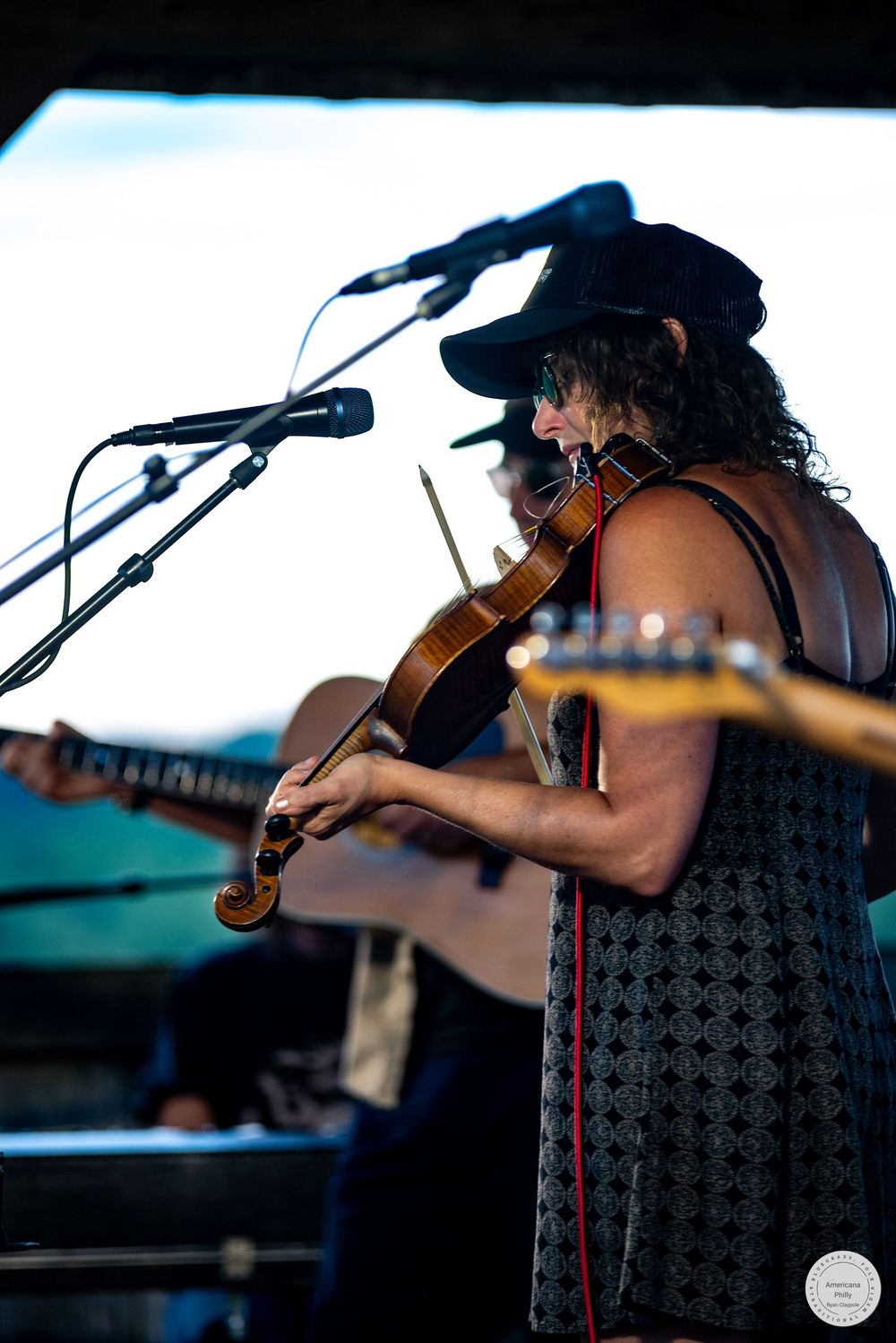 Woman in black hat playing violin on stage at outdoor music festival.