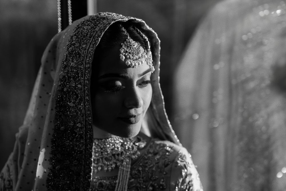 Black and white portrait of a bride in an ornate embroidered dupatta and jeweled headpiece, gazing softly to the side.