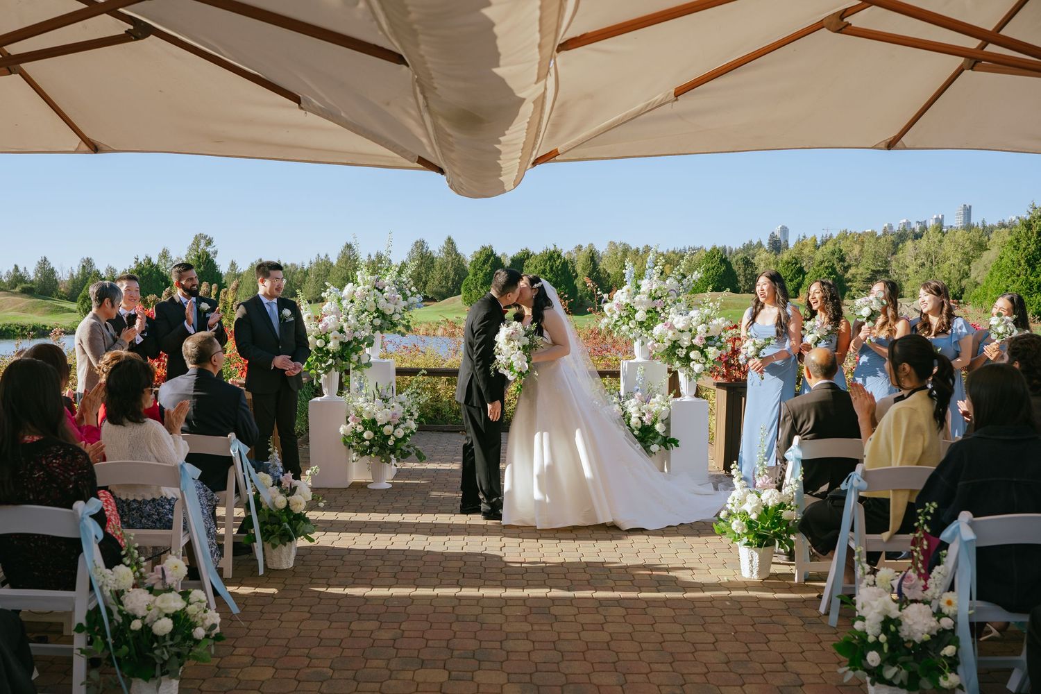Jennifer and Riley sharing their first kiss at the altar during their outdoor wedding ceremony at Riverway Clubhouse in Burnaby