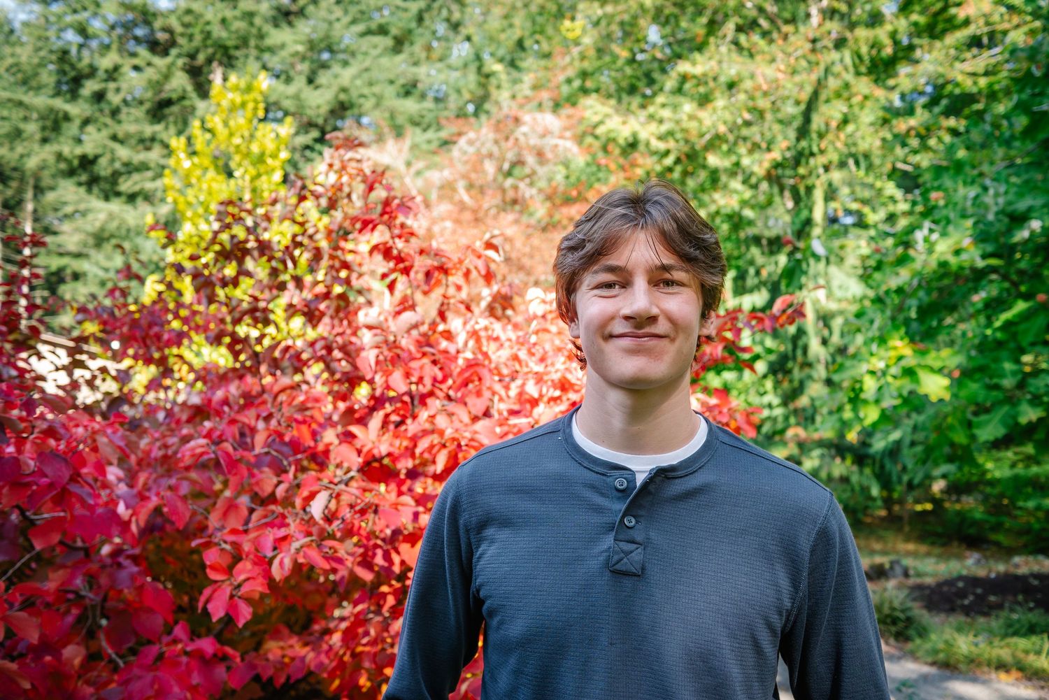 Smiling high school senior surrounded by bright red and orange fall leaves