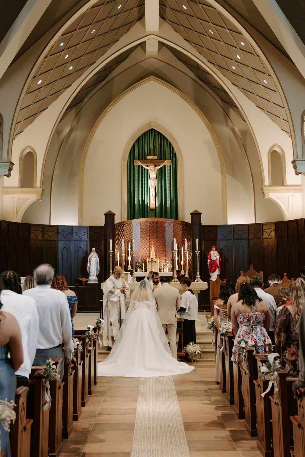 A bride and a priest stand at the altar during a Catholic wedding ceremony as guests watch from the church pews.